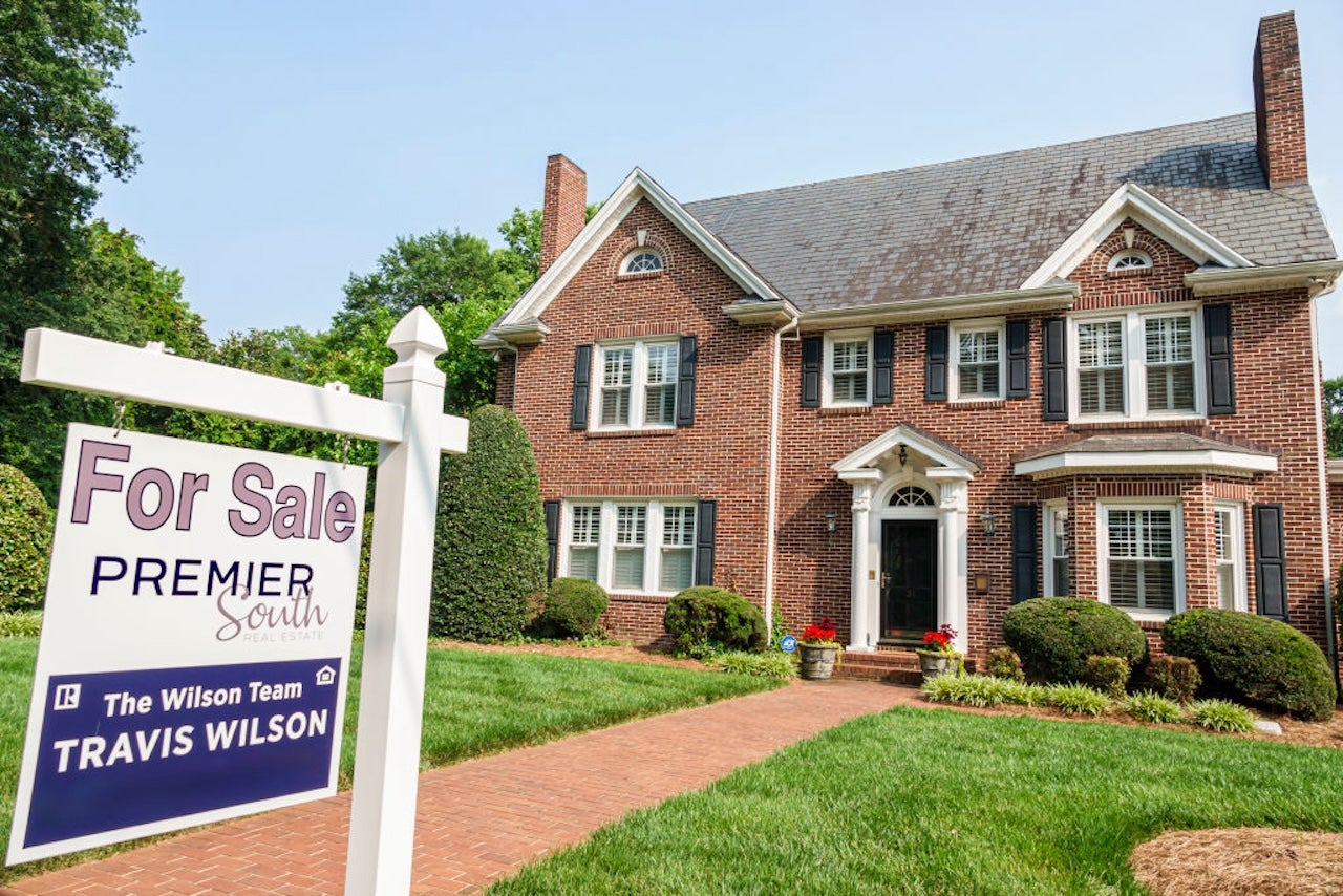 brick suburban home with for sale sign on front lawn