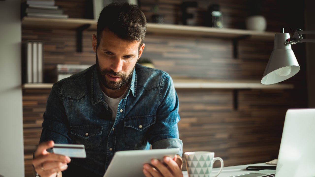 Man holding credit card while using digital tablet in the office.