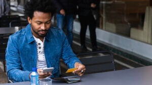 Mid adult man using credit card and smart phone for paying at sidewalk cafe