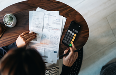 Overhead view of young woman calculating expenses while checking her bills with calculator.