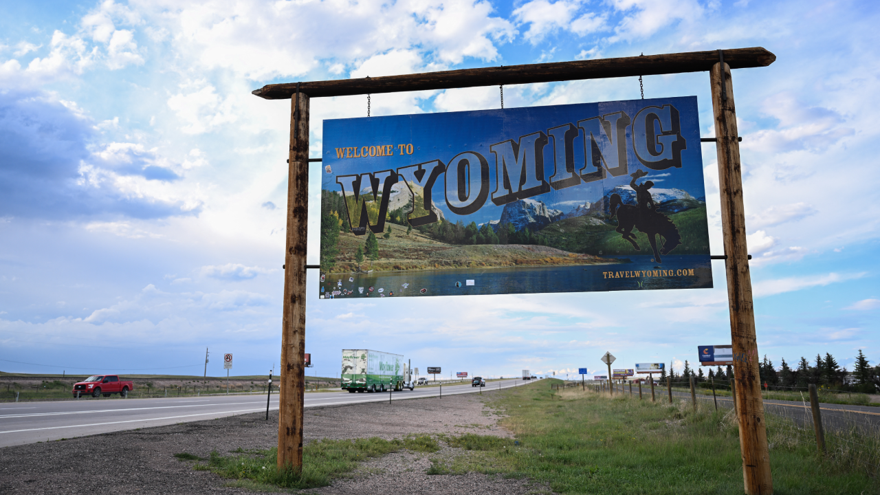 Cars and trucks drive past a Welcome to Wyoming sign south of Cheyenne, Wyoming