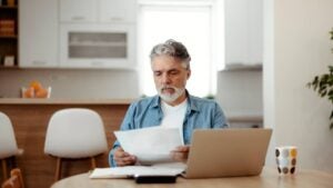 Older man looks at piece of paper at table.