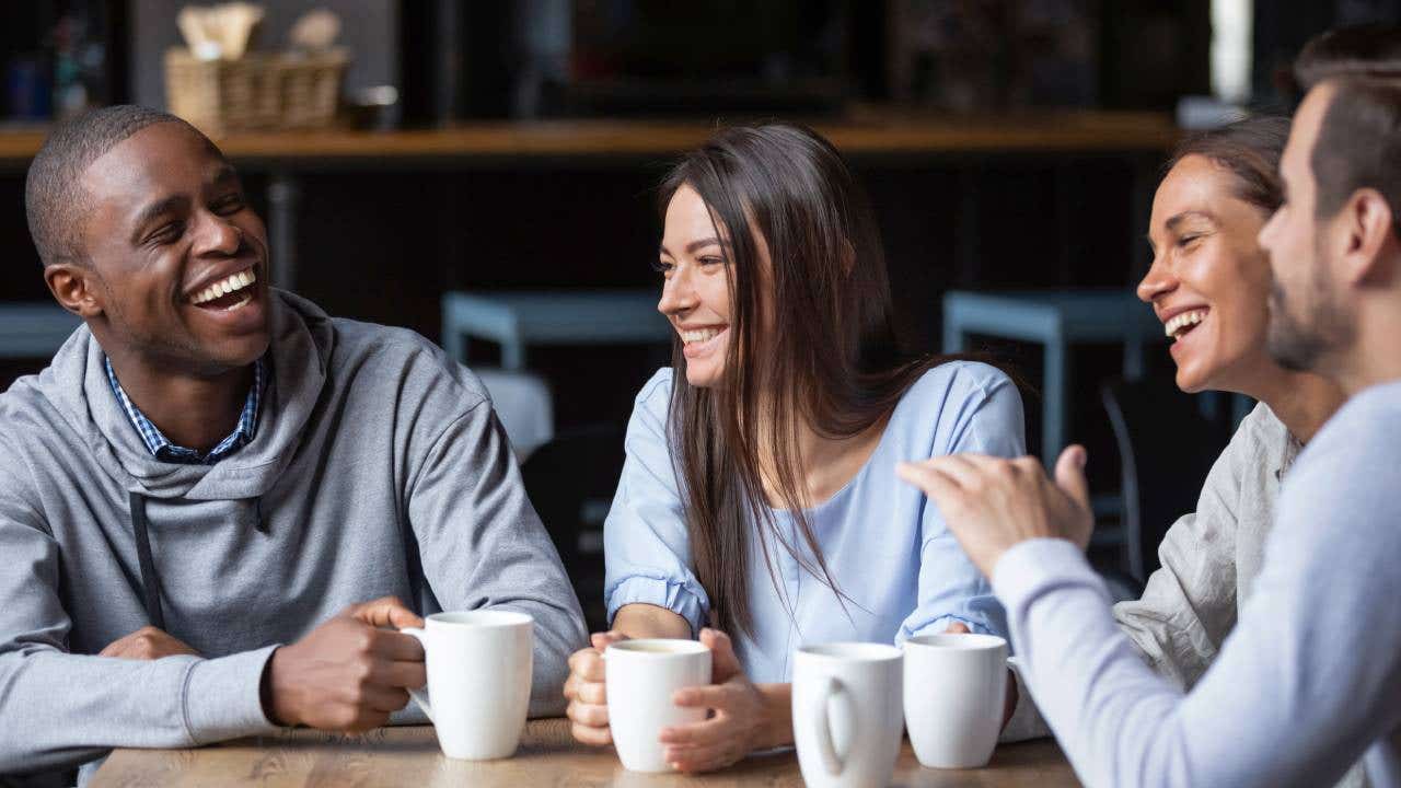 A group of millennial friends sit around a table drinking coffee.