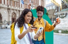 design image of two woman smiling and one is holding a credit card and phone in her hand