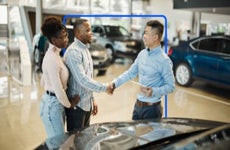 People looking at car and shaking hands while smiling