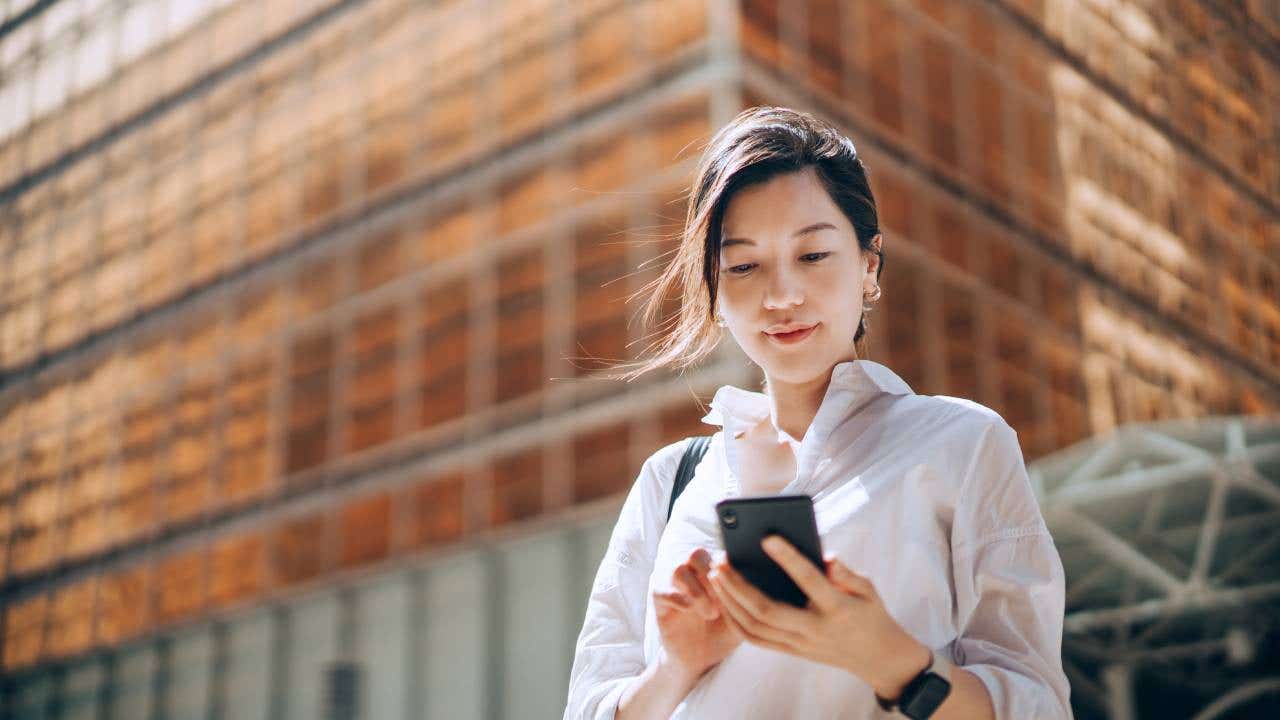 A woman looks at her phone outside.