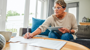 Mature woman using a digital tablet while going through paperwork at home.