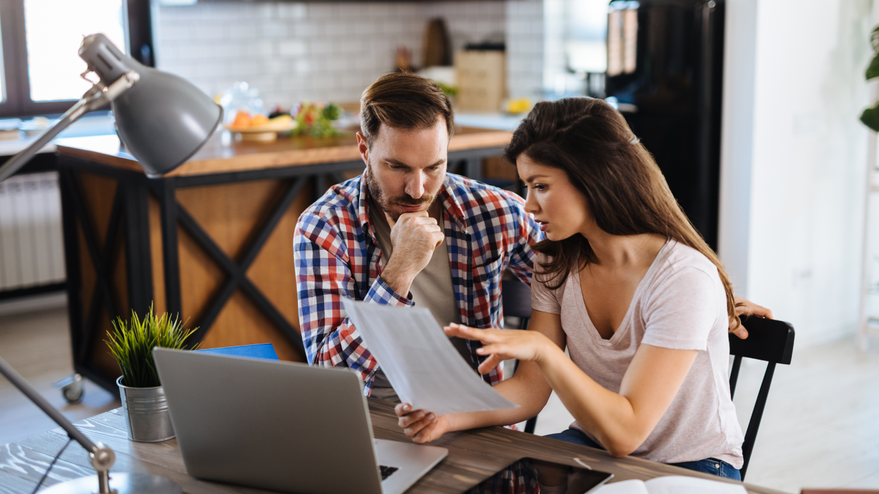 Frustrated couple checking bills at home using laptop.