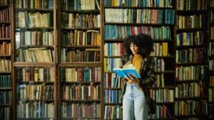 Wide shot woman reading book while browsing in antique bookstore