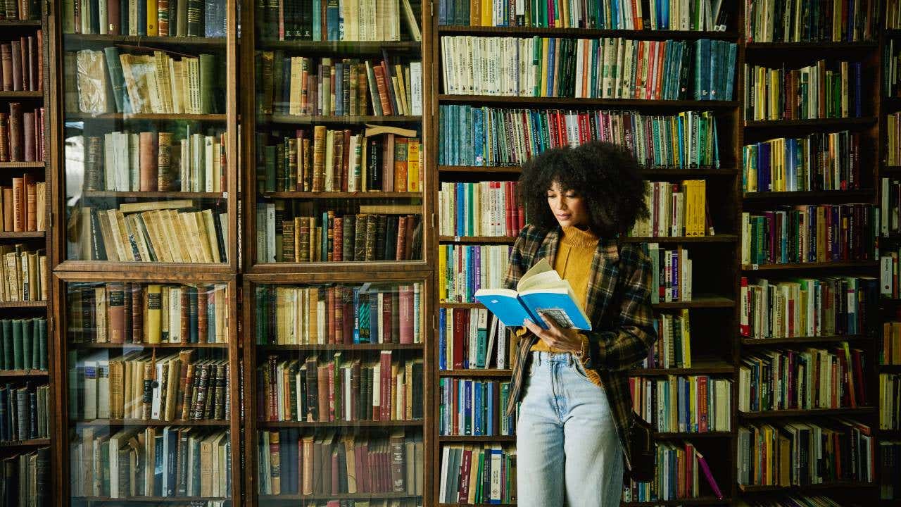 Wide shot woman reading book while browsing in antique bookstore