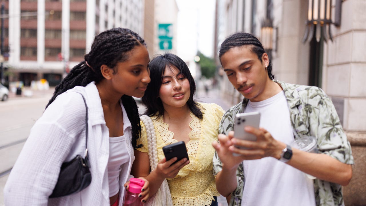 Three college age people looking at phones in city