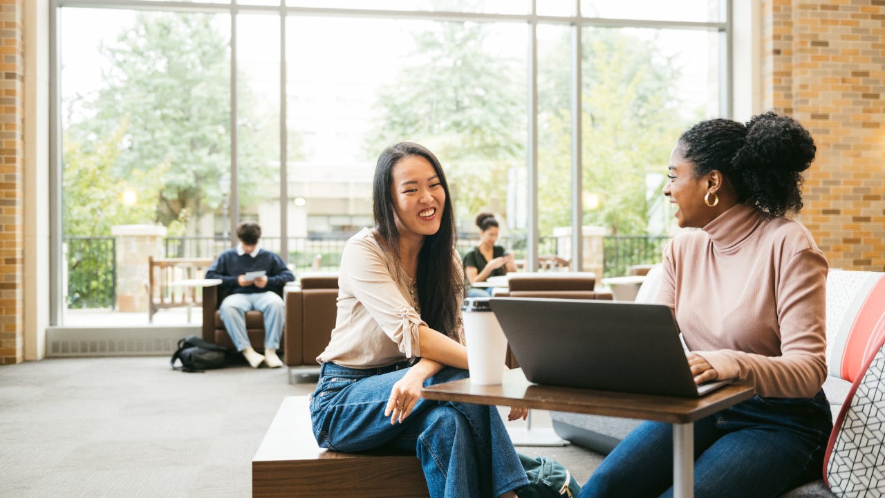 Two female university students sitting together smiling.