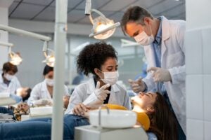 Teacher supervising a student examining a patient at dental school and explaining something to her