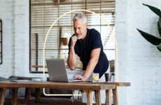 Image depicting a man learning over a desk, looking at his laptop