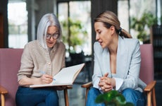 A retired woman consults with a younger woman while writing in a notebook.