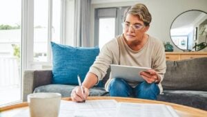 A woman uses a tablet at home while going through paperwork.