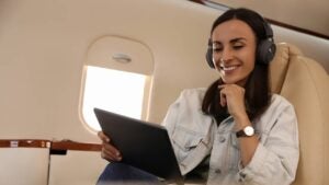 Young woman with tablet and headphones listening to music in airplane during flight