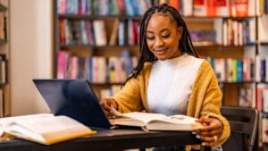 Young Black university student smiles while studying in a library.