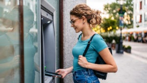 Young woman withdrawing money using phone at the ATM machine on the street in Budapest in Hungary.