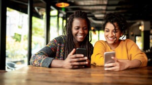 Two millenial friends using mobile phone.