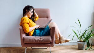 Young brown-haired female in eyeglasses, wearing yellow sweater sitting, relaxing and surfing net in office on break