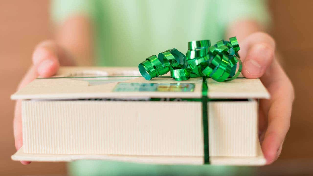 Outstretched hands holding a present with a green bow.