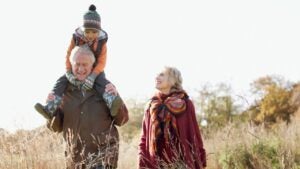 Grandparents carry their grandson on a walk through a field.