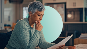 Profile view of a grey haired woman with her right hand on chin looking thoughtfully at a paper in her hand.