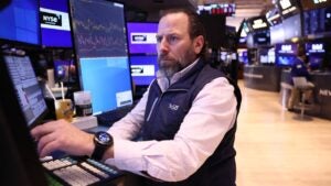 A trader on the floor of the New York Stock Exchange looking at at a monitor with a concerned look on their face.