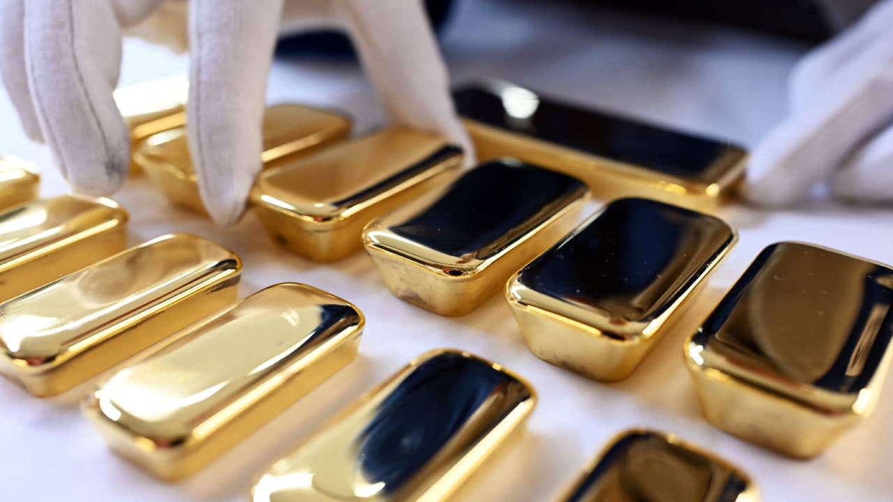 Gloved hands touching small gold bars lined up in rows.