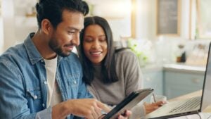 A couple works on a laptop and a tablet in their home.