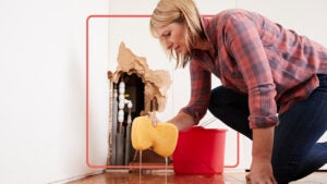 woman cleaning up leak coming from pipes inside a wall in her home