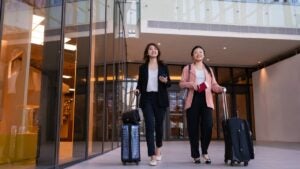 Two young Asian business women tourists walking with wheeled luggage in airport