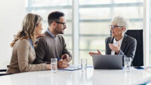 Senior agent talking to a couple in a meeting in an office.