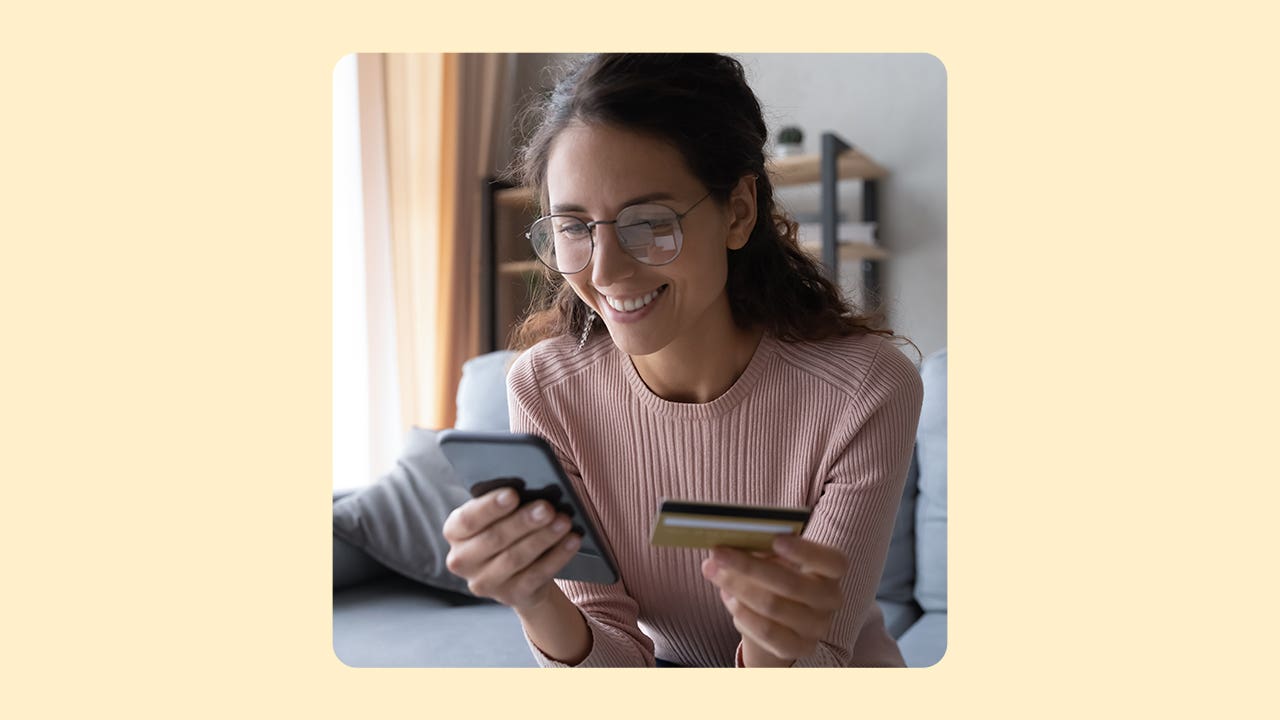 Woman holding a cell phone in one hand and a credit card in another.