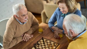 Happy mature friends playing chess at home