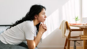 young woman looking away sitting on bed in the room