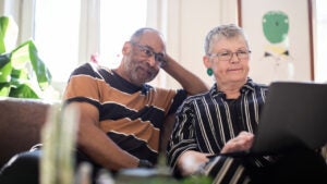 Woman using laptop while man sitting by on sofa