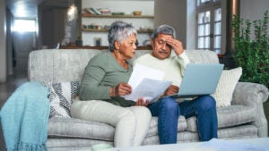 senior couple looking stressed while using a laptop and going through paperwork