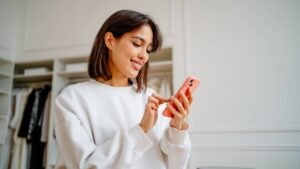 A businesswoman orders something on her phone while standing in a store.