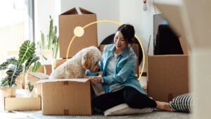 Woman sitting next to boxes. A dog is sitting inside an opened box