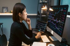 Person looking at stock charts displayed on two computer monitors.