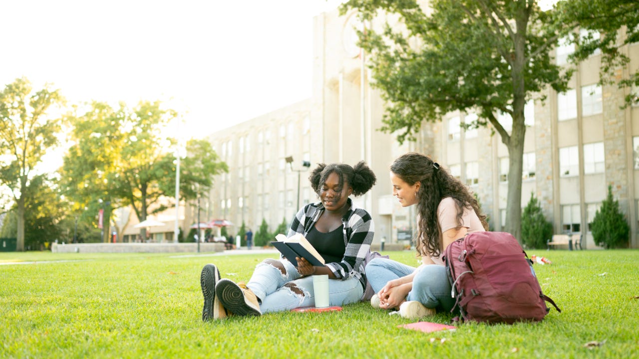 Two students sitting together on a university lawn studying and smiling