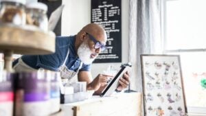 Storeowner leans over counter looking at tablet.