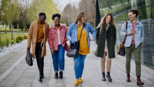 Group of five college students walking across campus together, smiling and talking.