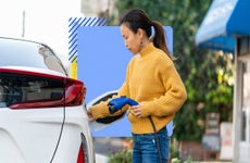 Asian person hooking up an electric plug-in to their electric car