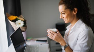 Woman looking at he laptop and smiling while holding a cup