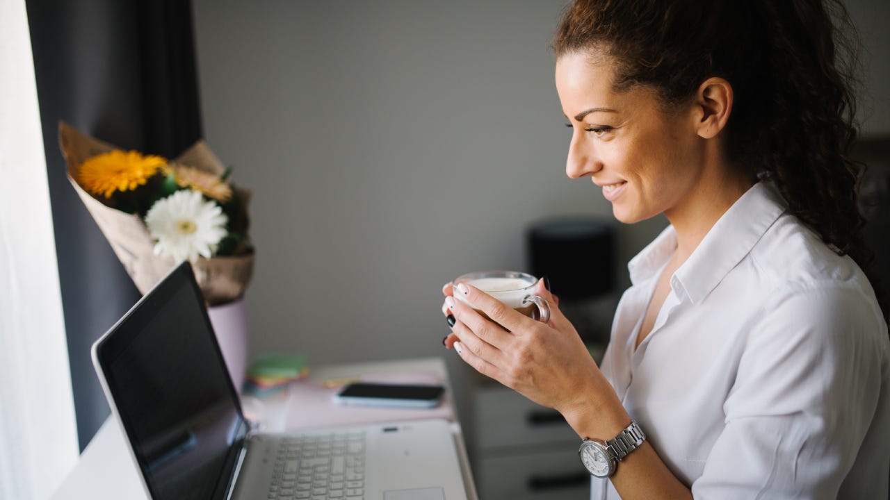 Woman looking at he laptop and smiling while holding a cup