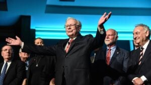 Warren Buffett standing on a stage with his arms flung out wide.