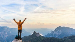 Happy hiker with raised arms on top of the mountain